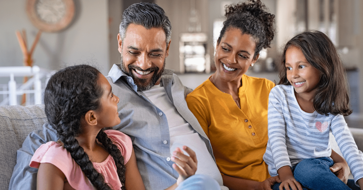 Smiling parents and two young girls sitting on a couch