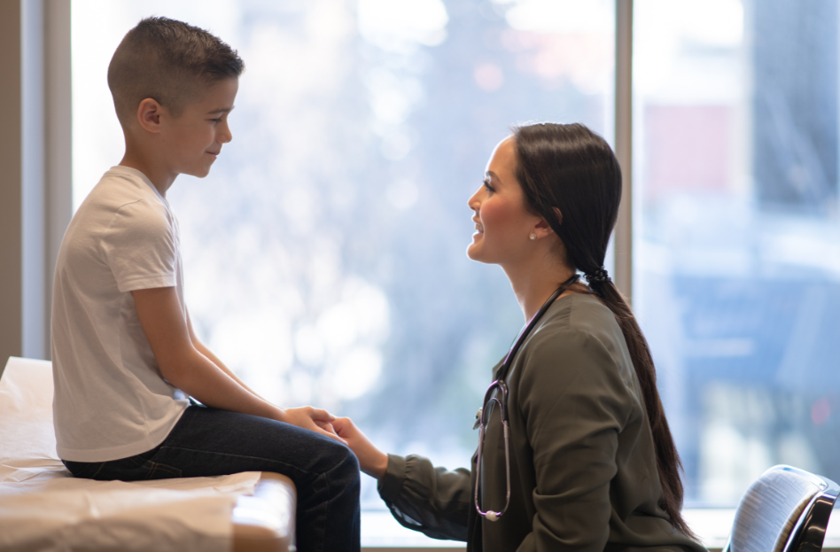 A pediatrician is sitting with and talking to a child.