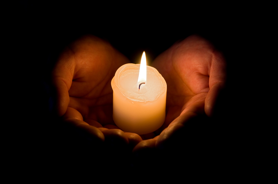 Someone holding a lit candle, the hands are lit, but the background is darkness.