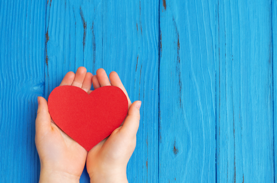 Hands cusped together, holding a red paper heart.